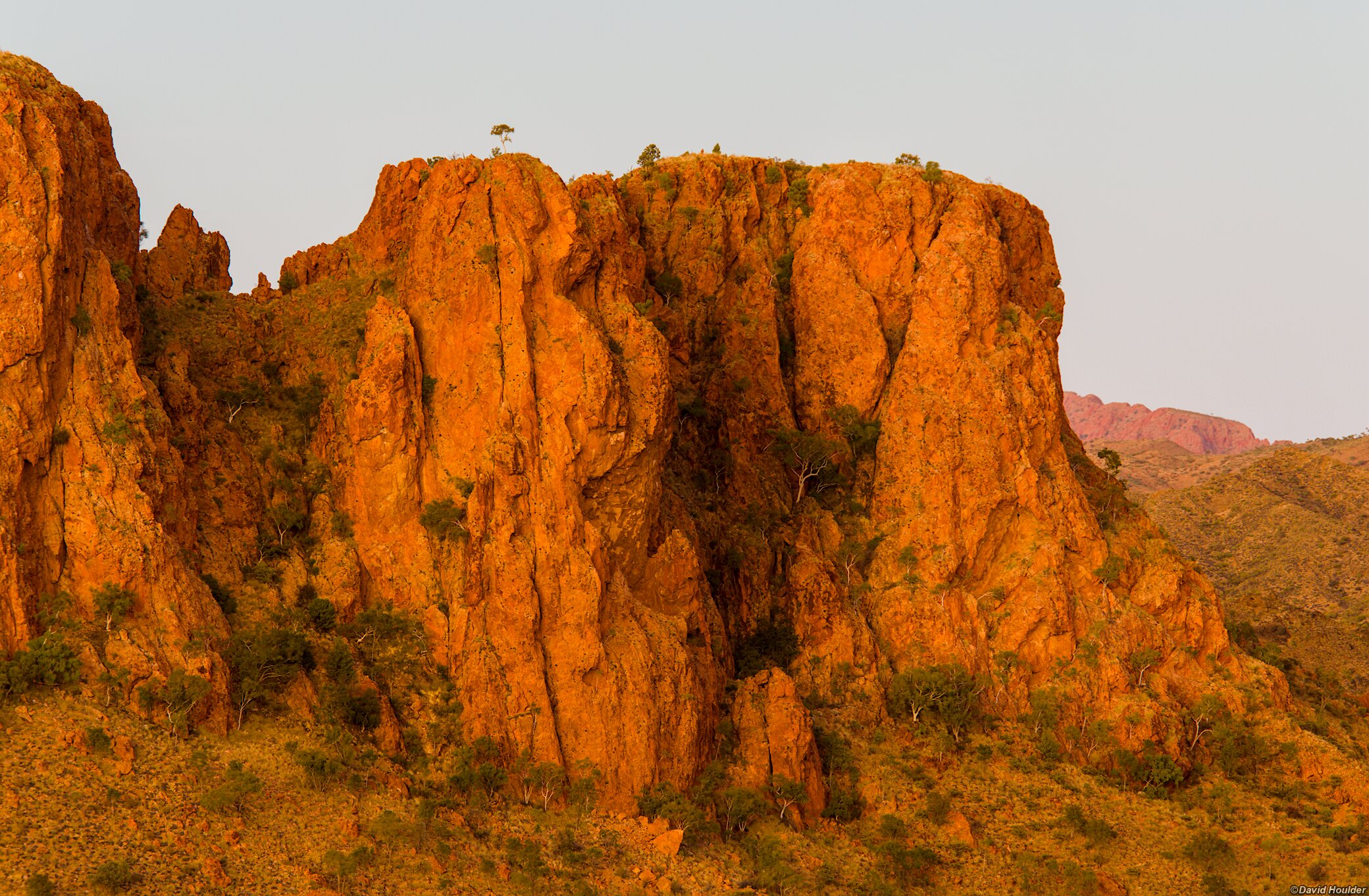 A rocky bluff and sparse vegetation with a clear sky in the background