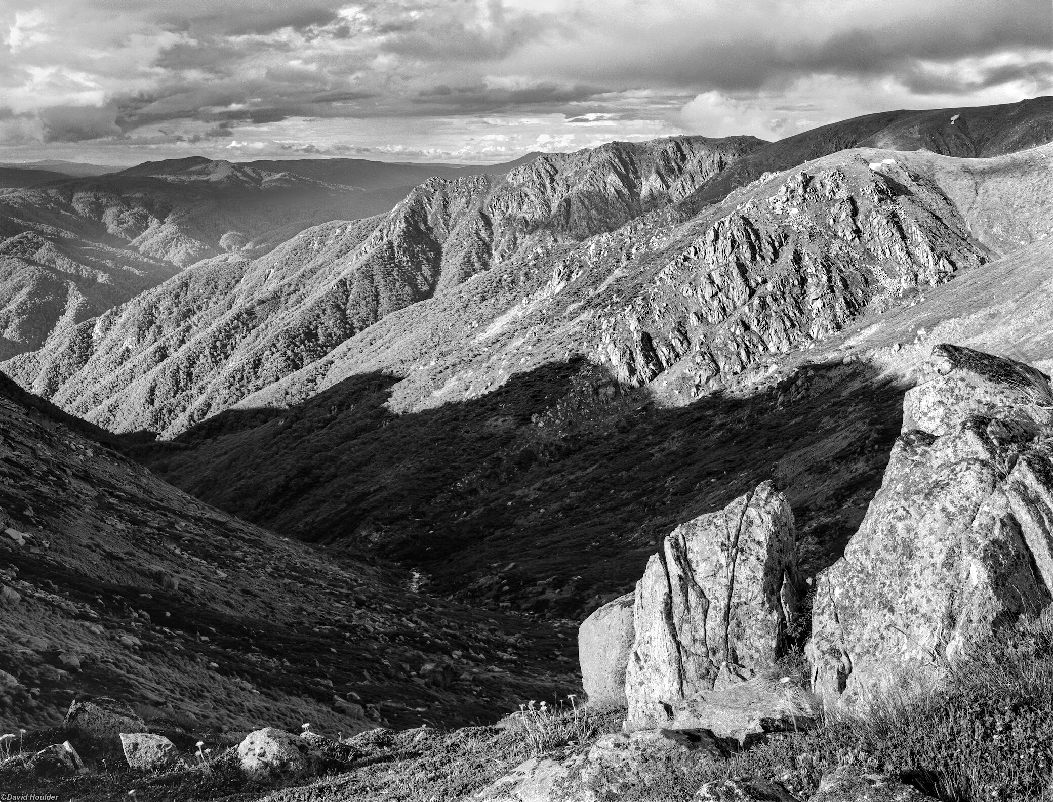 Shadows in a treeless alpine valley with sun-lit rocks in the foreground and background