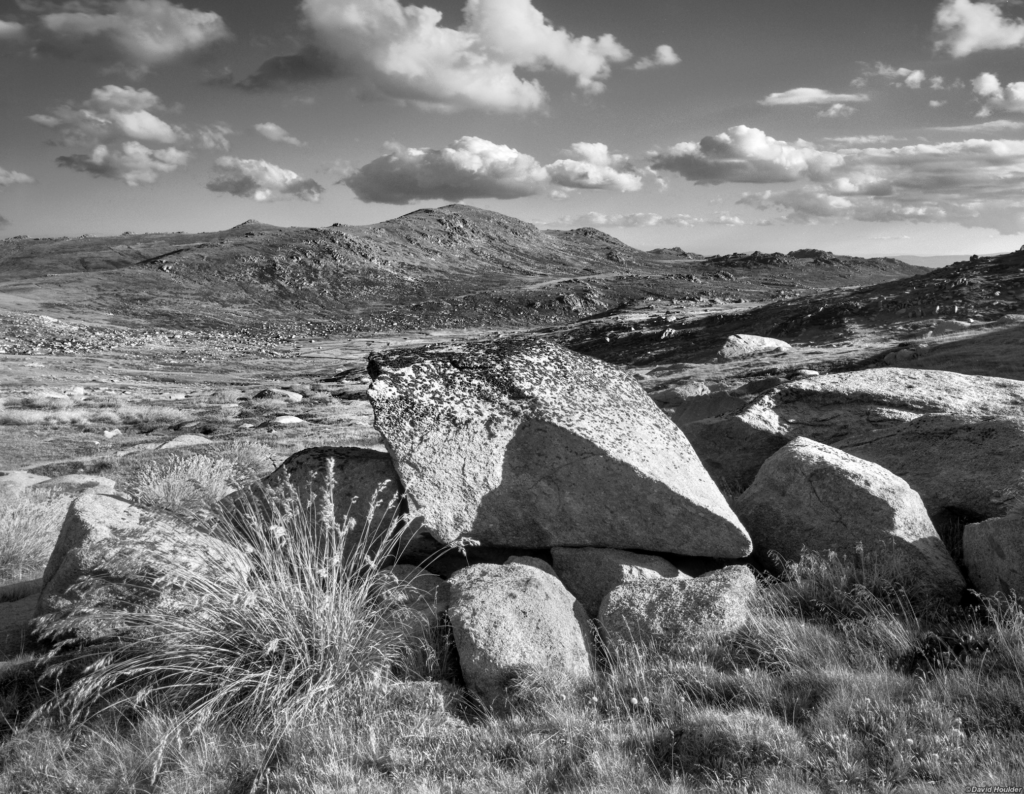 Jagged granite boulders and grasses, with Mt Kosciuszko and cloudy sky in the distance