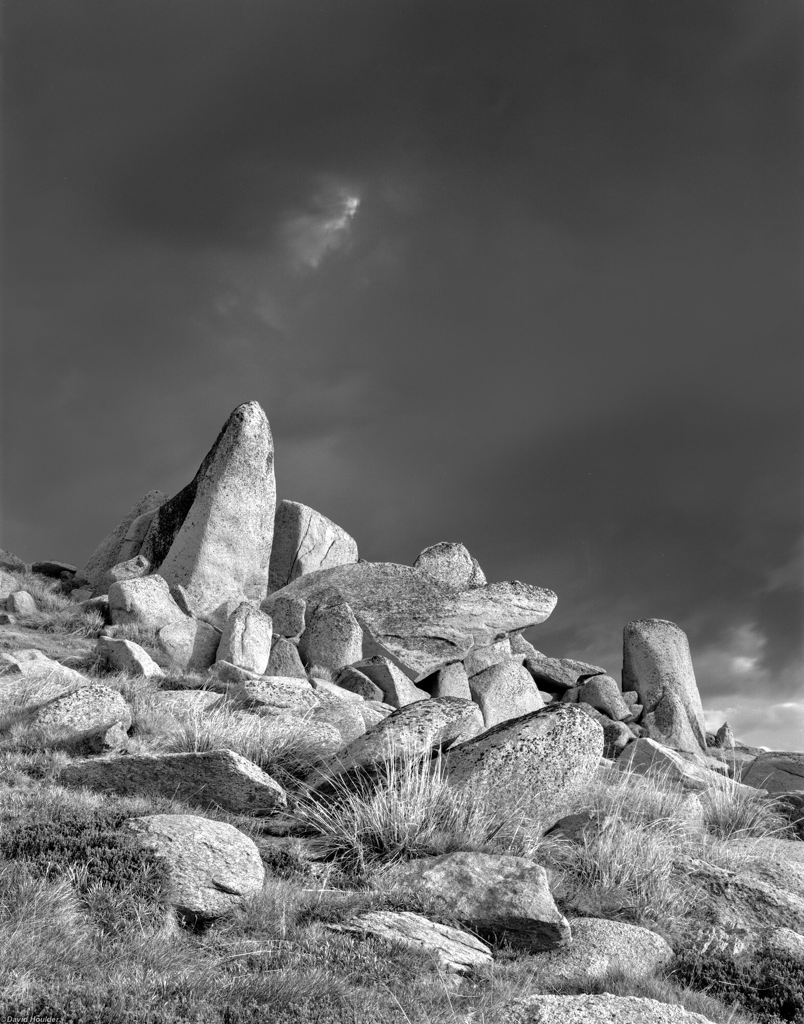 Angular granite boulders with grasses in the foreground and storm clouds behind.