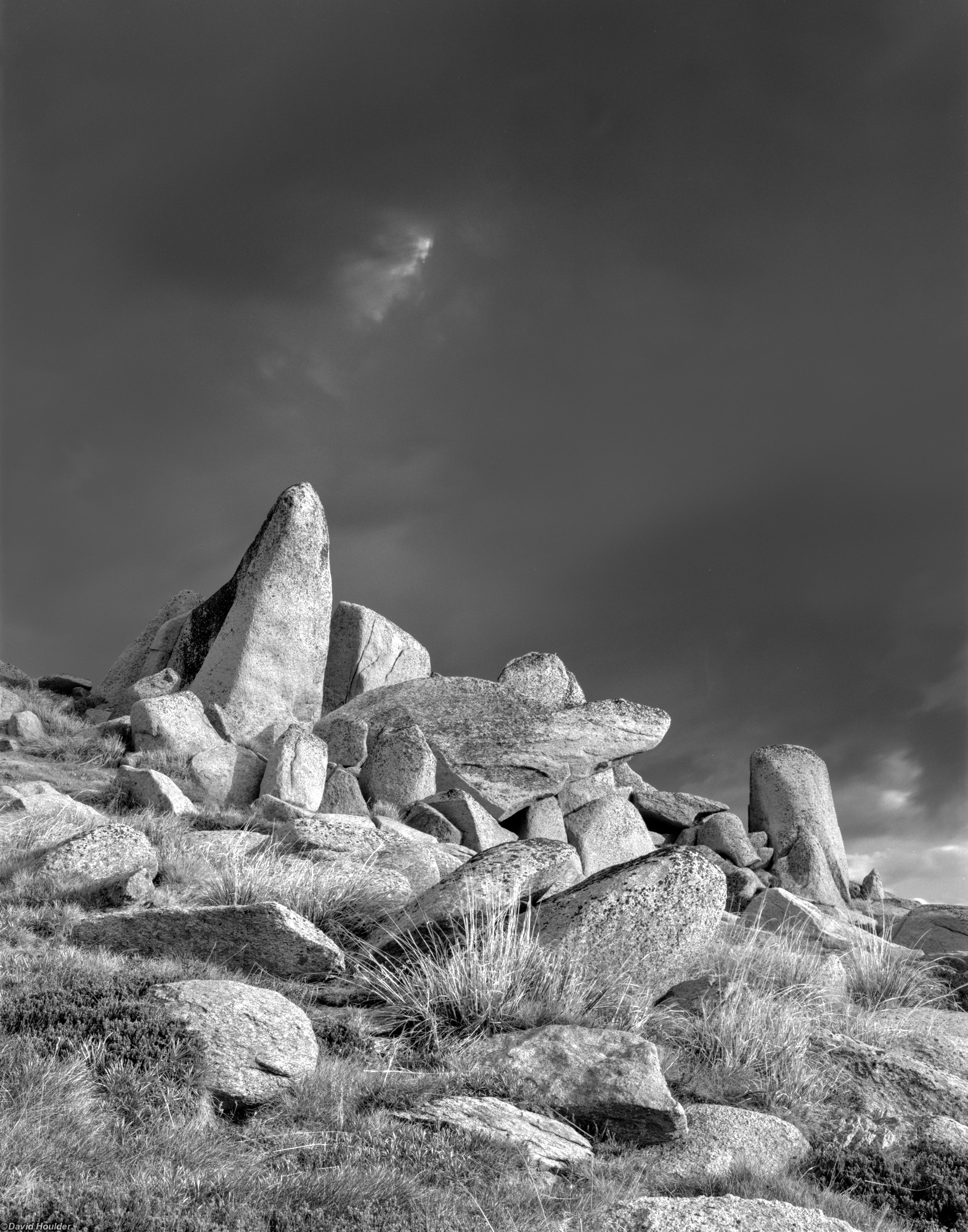 Angular granite boulders with grasses in the foreground and storm clouds behind.