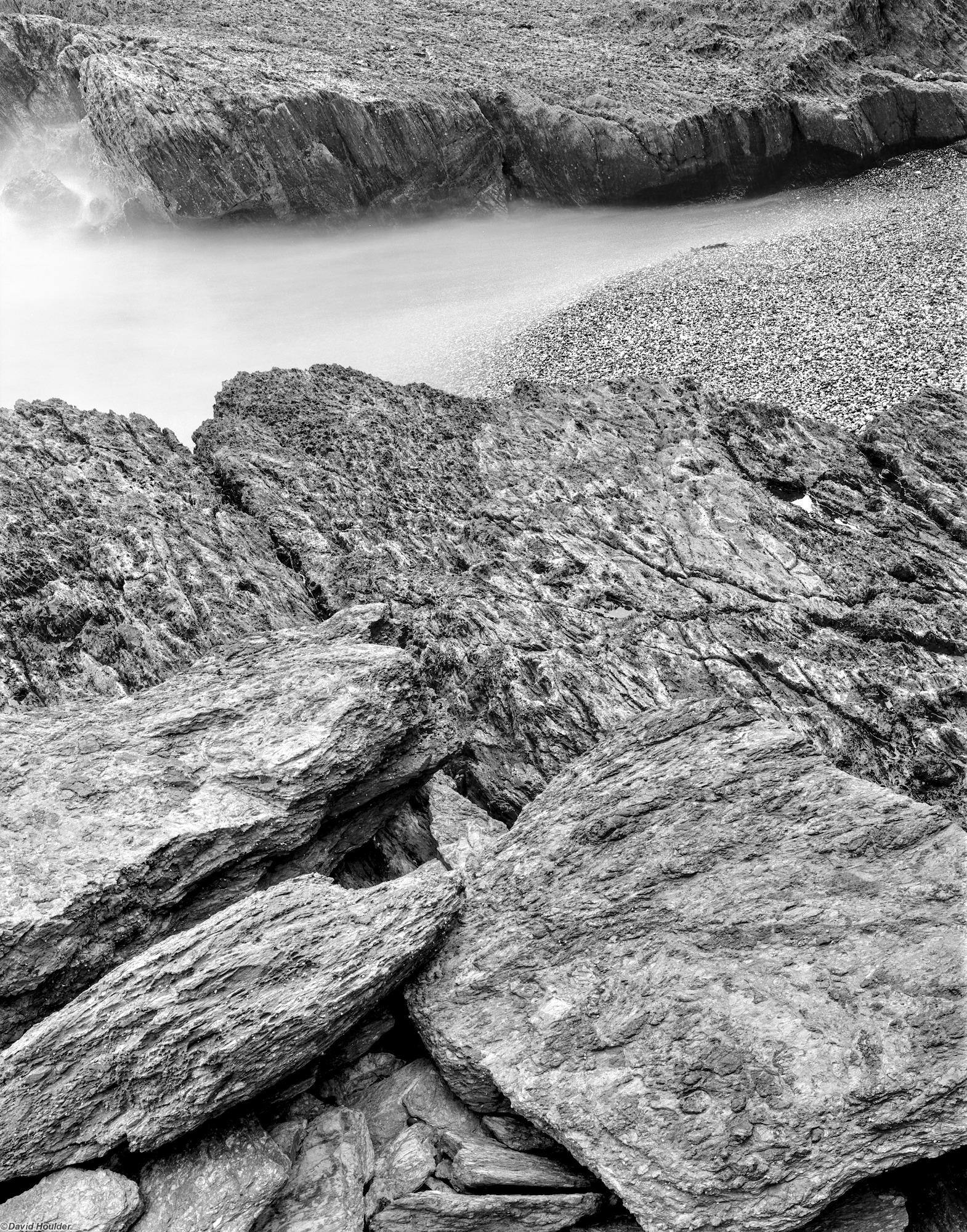 Jagged rocks, a tiny pebbly beach and motion-blurred water