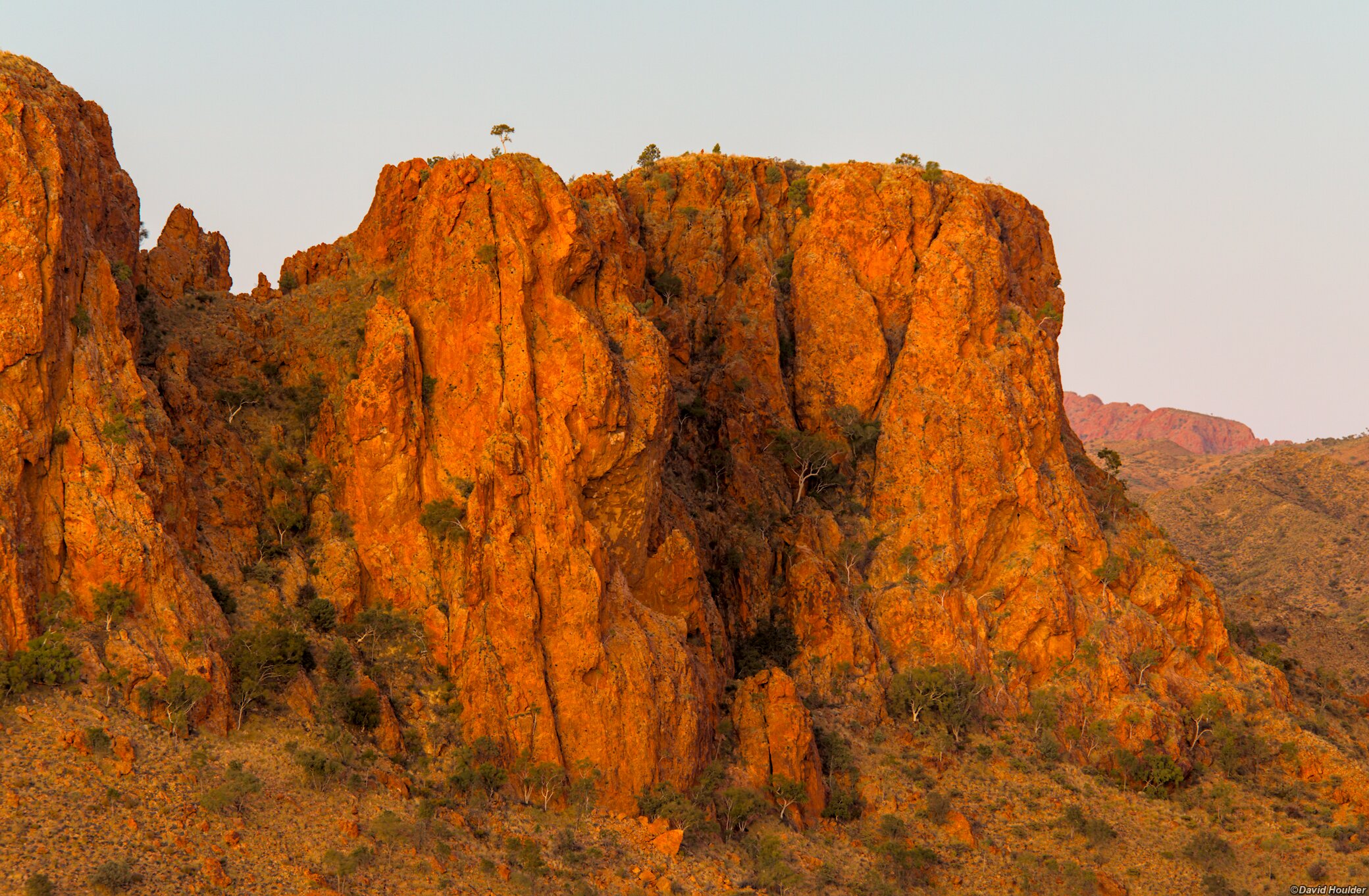 A rocky bluff and sparse vegetation with a clear sky in the background