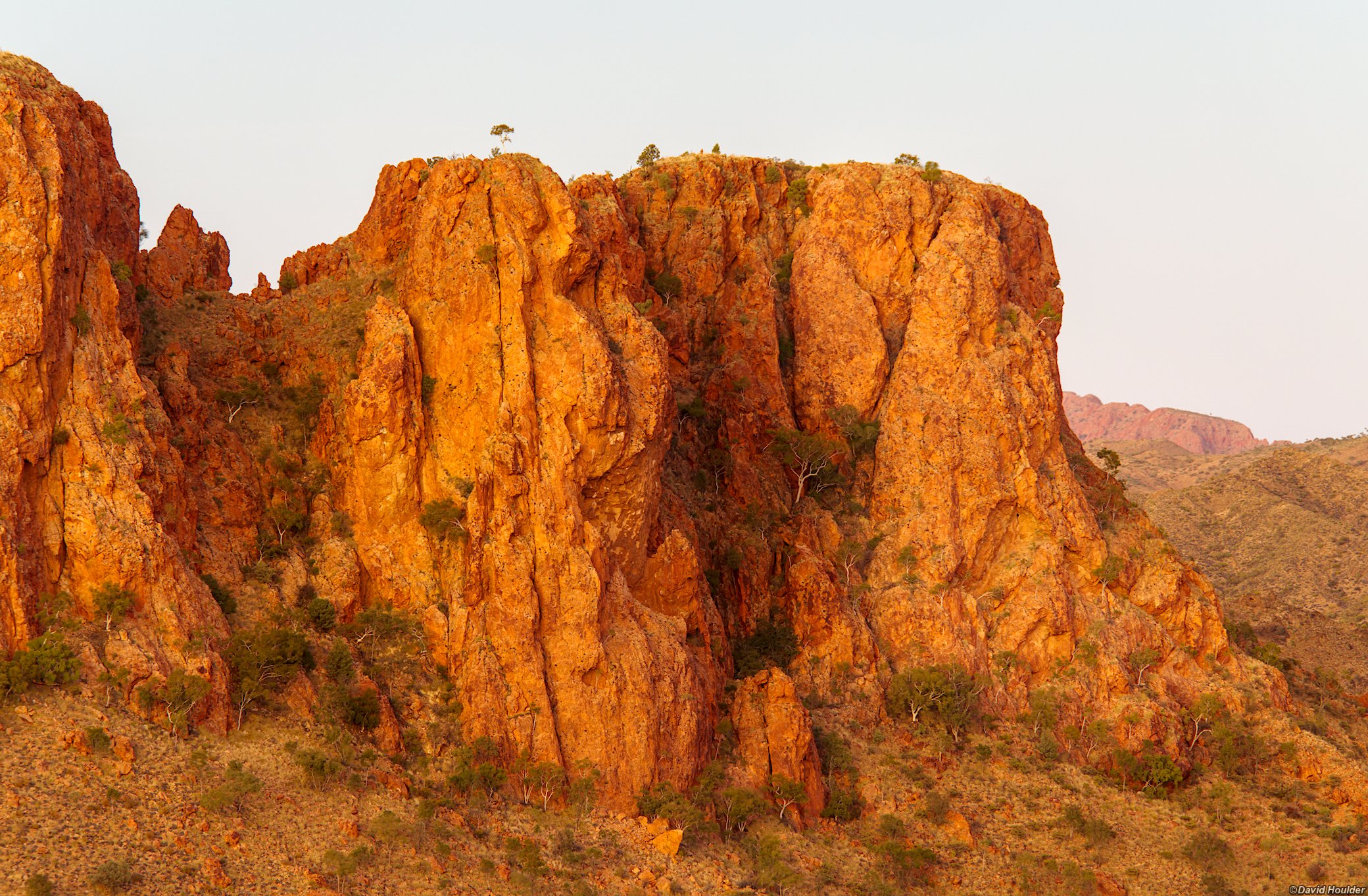 A rocky bluff and sparse vegetation with a clear sky in the background